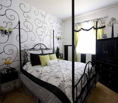 Wide view of smart chic bedroom with curvilinear mural on wall, black and white color scheme, iron bed frame, and dark furniture, and green room highlights.